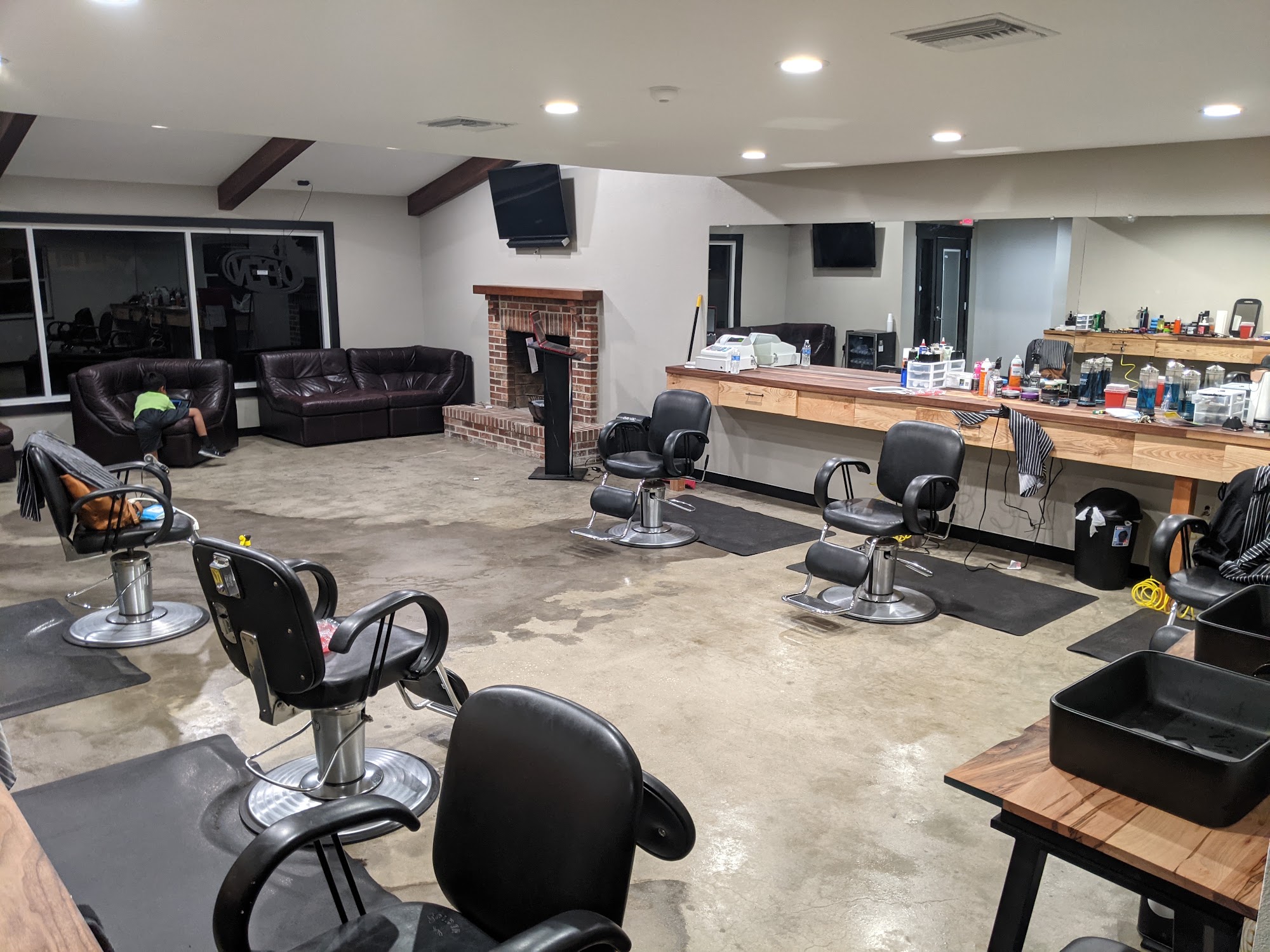 The main floor of Matt's Barbershop, barber chairs facing a long wood counter with leather couches and a brick fireplace behind